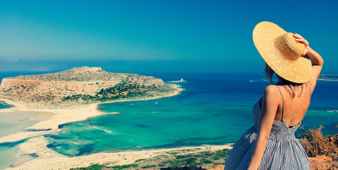 Young redhead girl in hat and dress with sea coastline on Balos, Crete, Greece - obrazy, fototapety, plakaty