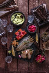 Assorted marinated fish on dark cutting board with vodka shots.