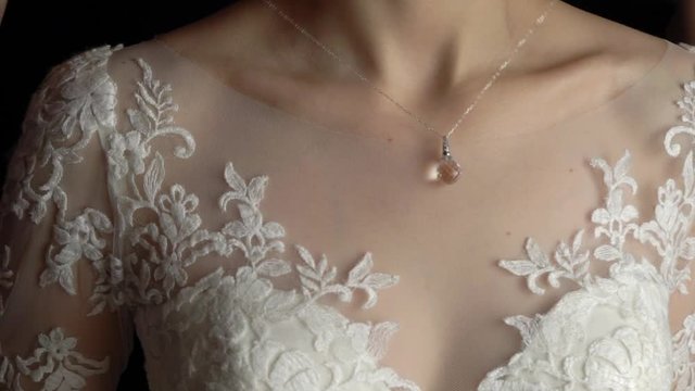 Wedding. Jewelry. The bride in a white dress putting on a necklace around her neck slowmotion
