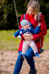 Young mother and a child on children's swing at playground in a park