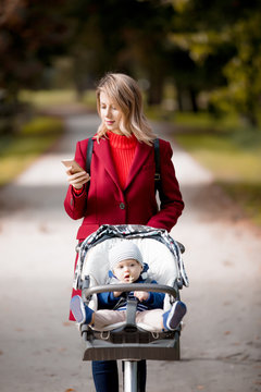 Young woman strolling in a park with stroller and a child in autumn season