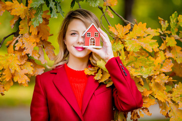 Young woman in red coat with house toy in autumn season park.