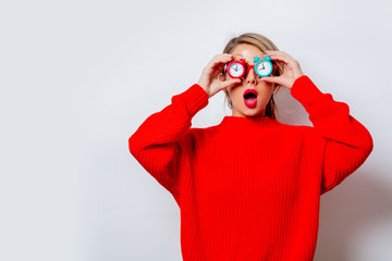 Portrait of a beautiful white woman in red sweater with little alarm clocks on white background,...