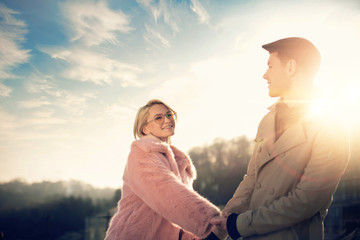 With you. Toned portrait of charming blond girl in pink fur coat sharing romantic moment with her boyfriend in flat cap. They looking at each other and smiling