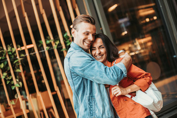 Portrait of cheerful man embracing outgoing girl while talking with her outdoor. Glad couple having fun together concept