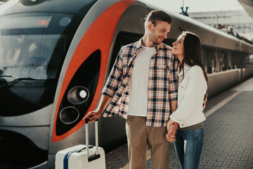 Positive male watching at smiling girlfriend with loving look while keeping arms together. They...