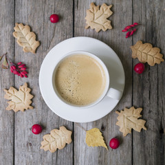 Cup of hot coffee, cookies in form leaves, dry autumn leaves, hawthorn and barberry fruits on a wooden background. Top view, flat lay