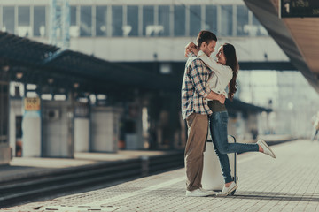 Full length side view beaming bearded man hugging positive female while locating outside on platform