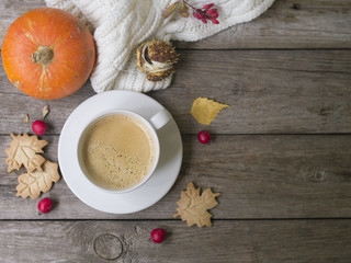 Coffee cup, knitted scarf, dry leaves, cookies, hawthorn and barberry fruits on a wooden background. Concept cozy atmosphere with a cup of coffee. Copy space, flat lay
