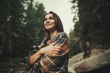 Attractive pleased young woman covering with warm blanket while resting in the forest