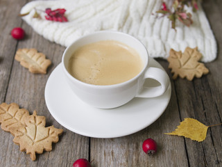 Coffee cup, knitted scarf, dry leaves, cookies, hawthorn and barberry fruits on an old wooden background. Concept cozy atmosphere with a cup of coffee. Selective focus
