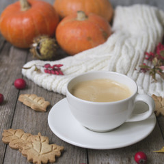 Coffee cup, knitted scarf, dry leaves, cookies, pumpkin, chestnuts, hawthorn and barberry fruits on a wooden background. Concept cozy atmosphere with a cup of coffee. Copy space, selective focus