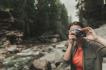 Pleasant young woman making photos while spending time in the forest