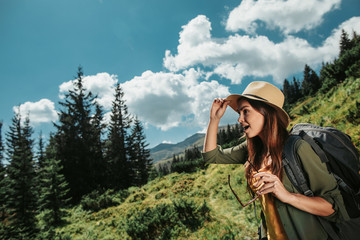 I am impressed. Side view portrait of pretty girl touching hat while looking away with surprised expression. Beautiful view of sky, trees and plants on background