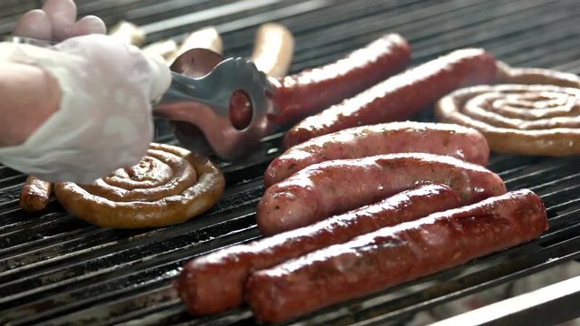 Grilling sausages, hand with tongs. Delicious meat products.