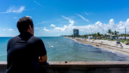 Young man looking at the view of Dania beach in Miami, Florida. Summer sunny day with many people swimming in the water