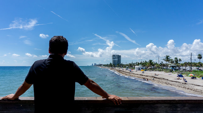 Young man looking at the view of Dania beach in Miami, Florida. Summer sunny day with many people swimming in the water