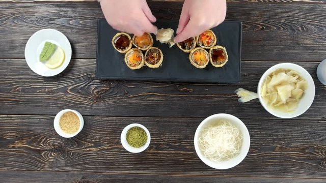 Hands preparing sushi, ginger. Unagi maki rolls on plate.