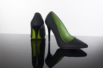  pair of pointed woman shoes with black soles green high heels on reflective floor