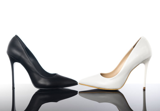 Black and white high heels pointed woman stiletto shoes on reflective floor.