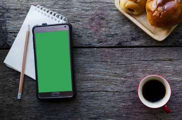 Smart phone with green screen and notepad with pencil and red coffee cup on wood backgrounds above - Powered by Adobe