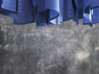 Hanging blue shirts tail with slightly blurred cement wall background.