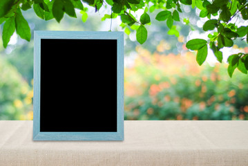 Blank vintage chalkboard standing on table over blur outdoor nature background, space for text, mock up, product display montage
