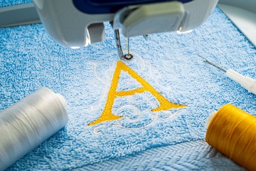 Alphabet logo design on towel in hoop of embroidery machine
