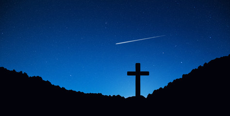 Silhouette of crucifix cross on mountain at night time with star and space background.