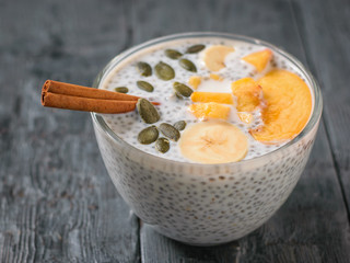 Chia seed pudding with peach, pumpkin seed and cinnamon on a dark wooden table.