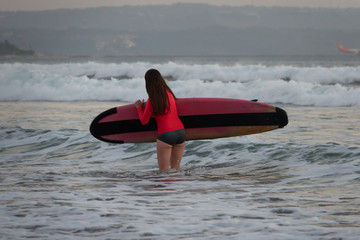 A beautiful girl standing with surfboard in a sea