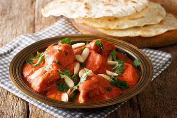 Traditional recipe for butter chicken Murgh Makhani in spicy sauce with almonds and cilantro close-up with roti. horizontal