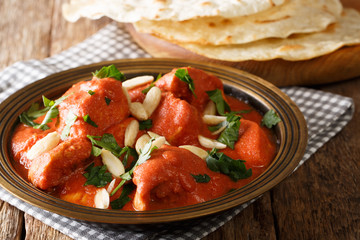 Indian popular food Butter Chicken Murgh Makhani with spicy sauce, almonds and cilantro close-up on a plate with bread roti on the table. horizontal