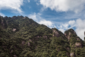 forest covered slope of Mount Sanqing under the cloudy blue sky