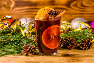 Cup of mulled wine with cinnamon, christmas decorations and fir tree branches on wooden table