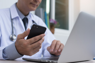 Doctor using smartphone and working on laptop computer
