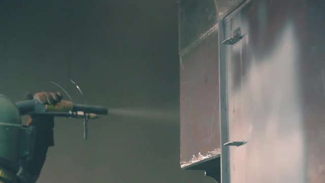 Man cleans metal surface by sandblaster gun in a metal construction factory. Shotblaster in a process