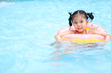 Fototapeta na wymiar Asian child or kid girl swimming wear life ring because can not swim and smile with happy fun on swimming pool or water park for refreshing and relax with exercise at summer holiday travel in resort