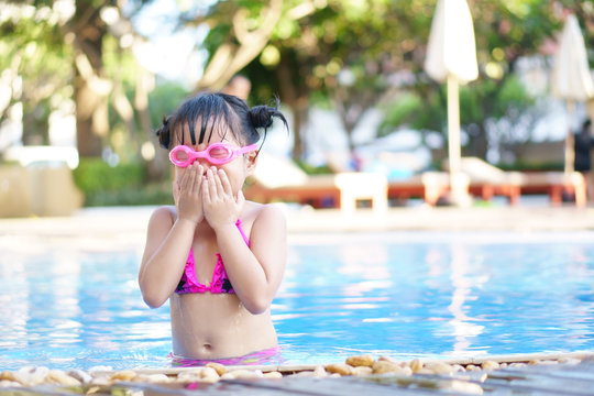Asian child cute or kid girl wear pink bikini and goggles for swimming and choke water with happy fun on swimming pool or water park and nature for refreshing and relax with exercise on summer holiday