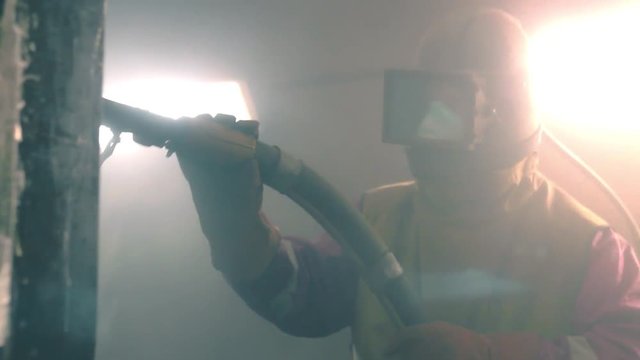Man cleans metal surface by sandblaster gun in a metal construction factory. Shotblaster in a process