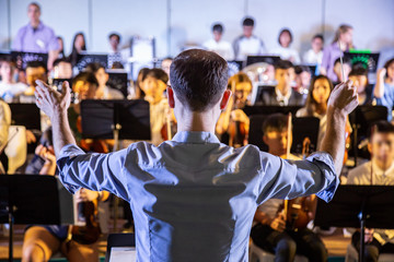 Male school conductor conductiong his student band to perform music in a school concert - obrazy, fototapety, plakaty