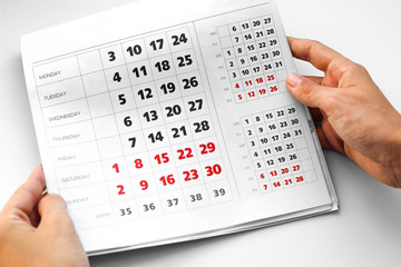 Hand holding the calendar. White calendar. Weekends are highlighted in red. Close up