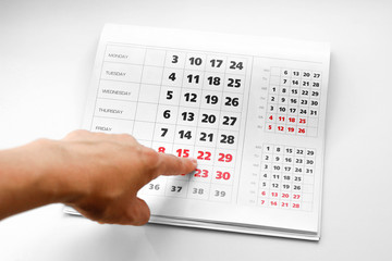 Hand pointing to the calendar. White calendar. Weekends are highlighted in red. Close up