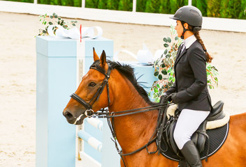 Beautiful girl on sorrel horse in jumping show, equestrian sports. Light-brown horse and young...