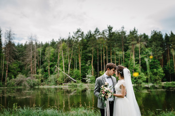 Portrait of an attractive groom looking bride on nature in the park. Wedding ceremony near lake. Happy and joyful moment.
