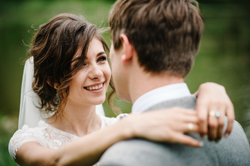 Fototapeta premium Portrait of an attractive groom looking bride on nature in the park. Wedding ceremony near lake. Happy and joyful moment.