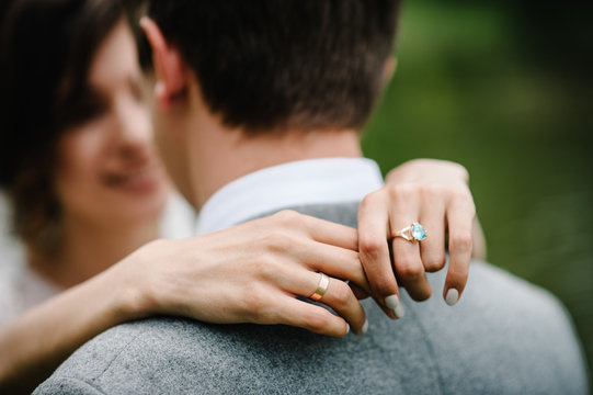 View of hands with wedding rings. Wedding day. Portrait of an attractive groom hugs bride on nature in the park. Happy and joyful moment. Romantic couple of newlyweds.