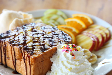Honey toast ice cream with mix fruit sliced and whipped cream served on white plate over wooden table