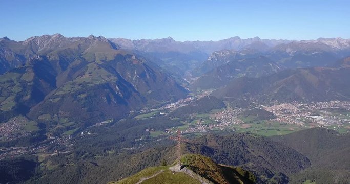 4K Drone aerial view to the Seriana valley and Orobie Alps in a clear and blue day. The cross at the top of the mountain. Landscape from Pizzo Formico Mountain, Bergamo, Italy