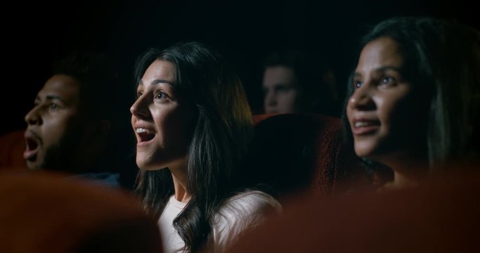 Movie theatre audience watching a movie. Focus on young woman who reacts with amazement during a scene